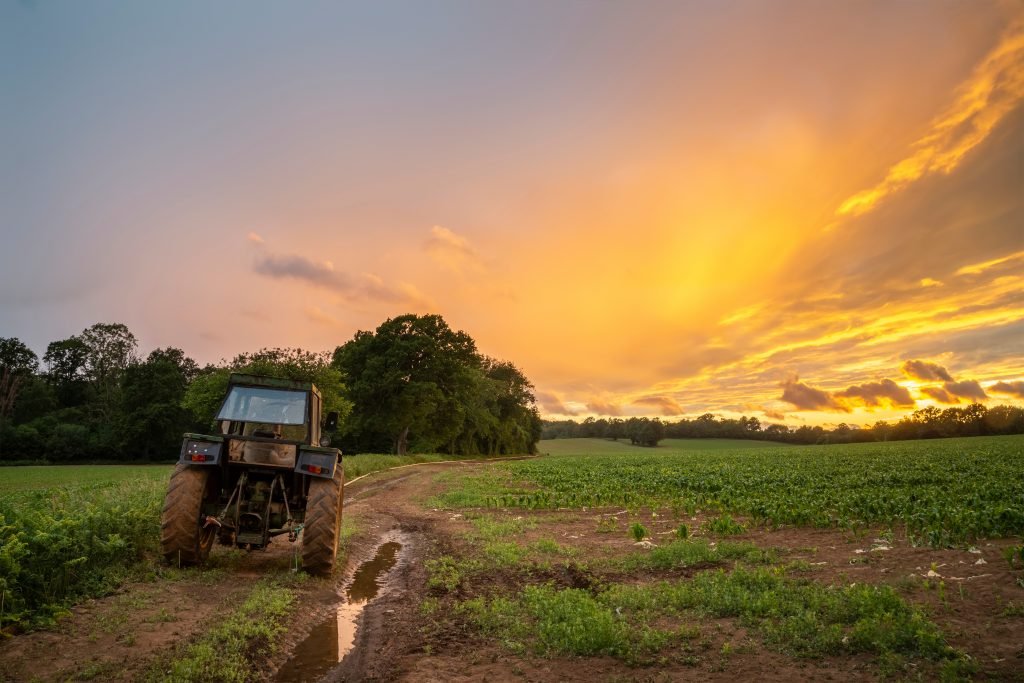 The photo depicts a British farm. A tractor is stationary in a field with the sun setting in the background.