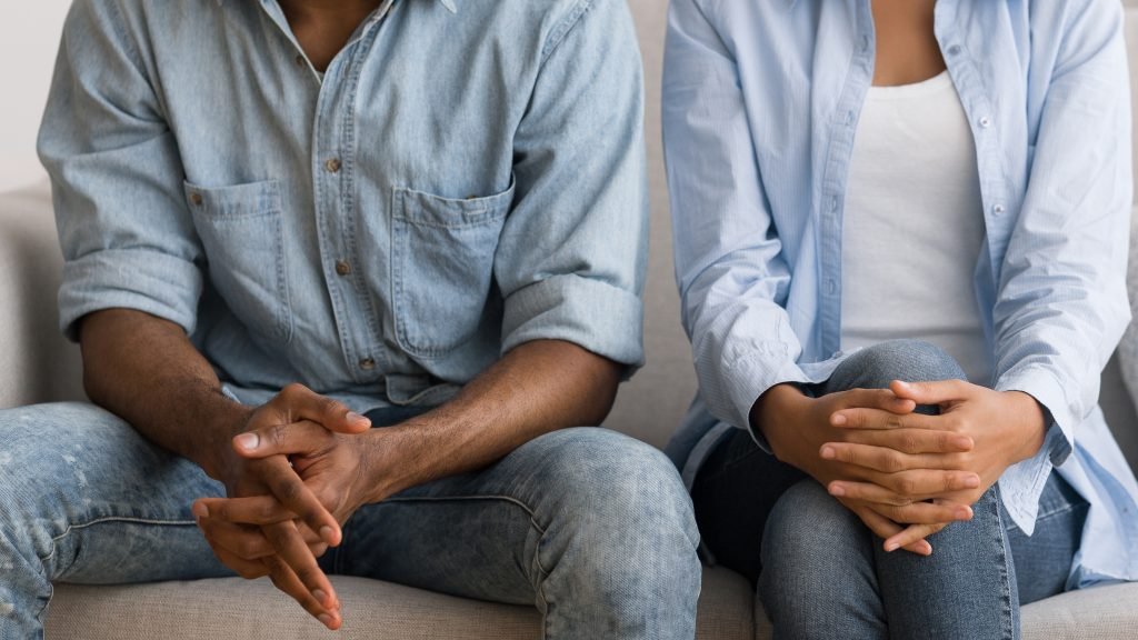 A photo of a couple sat side by side. Their body language is closed off. Their faces are out of shot.