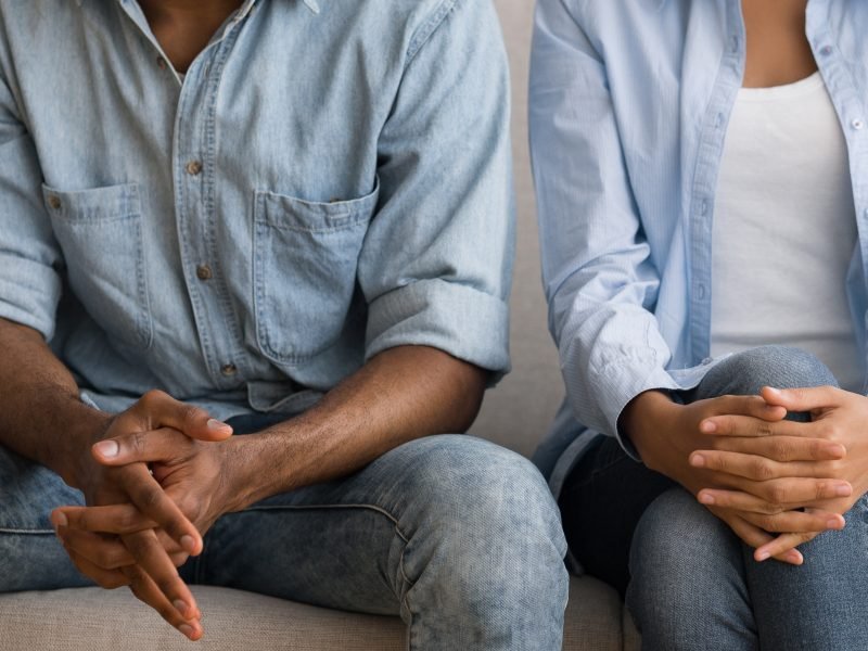 A photo of a couple sat side by side. Their body language is closed off. Their faces are out of shot.